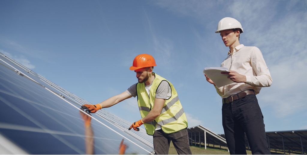 An engineer with a clipboard and a worker in a safety vest inspect a large ground-mounted solar panel array.