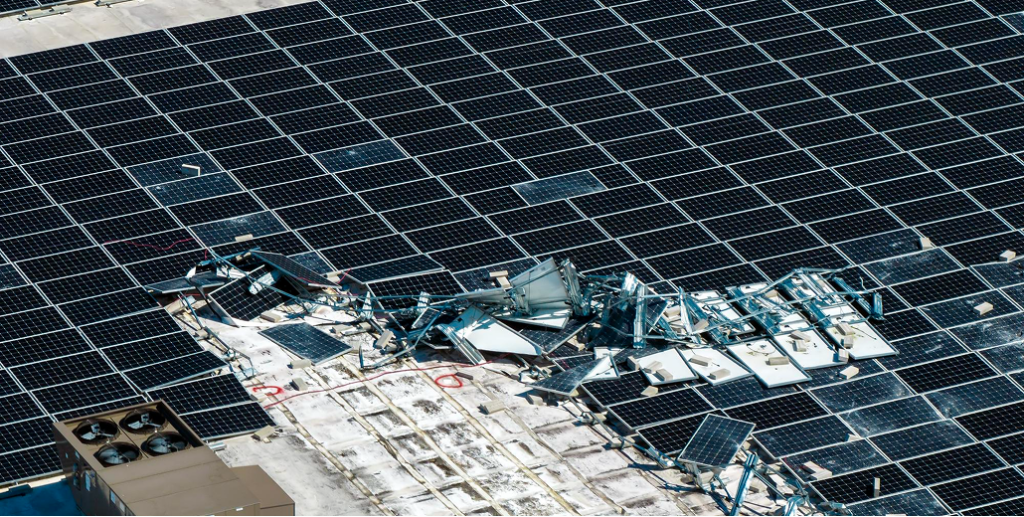 Aerial view of a commercial solar array with a heavily damaged, collapsed section of twisted metal and broken panels.