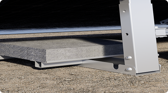 A grey ballast slab rests on a silver metal frame, connected to a vertical support post of a solar panel mount on the ground.