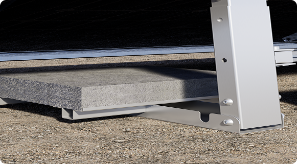 A grey ballast slab rests on a silver metal frame, connected to a vertical support post of a solar panel mount on the ground.